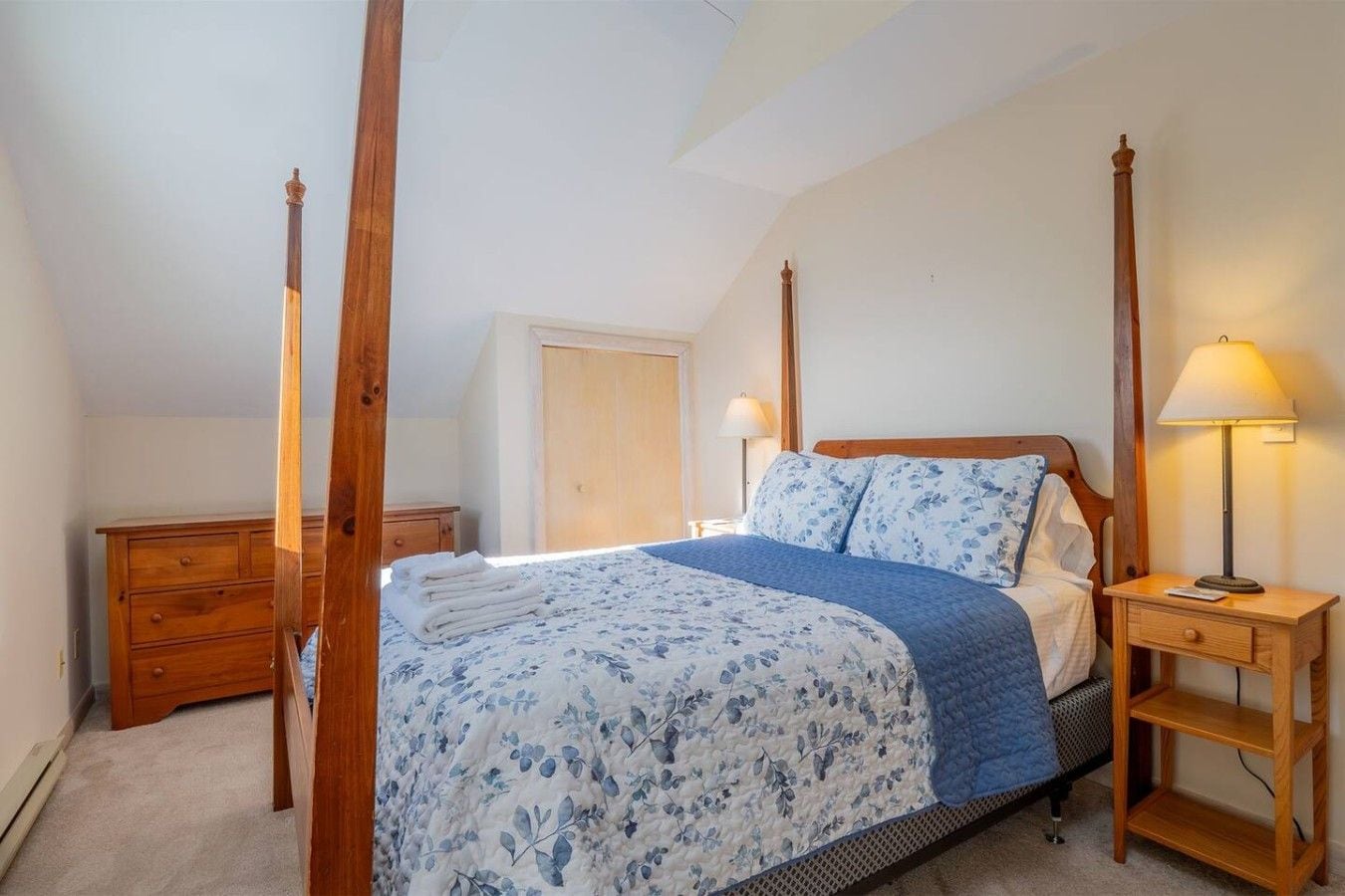 A bedroom with a four-poster bed, a wooden nightstand, a dresser, and a door in the background.