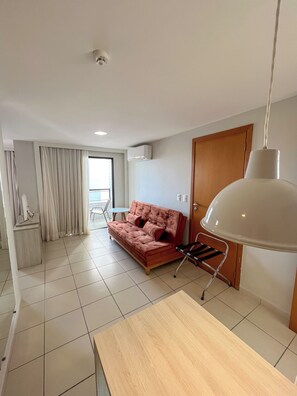 A modern living room with a sofa, a table, and a hanging lamp. - Flats Vista Mar (Natal)