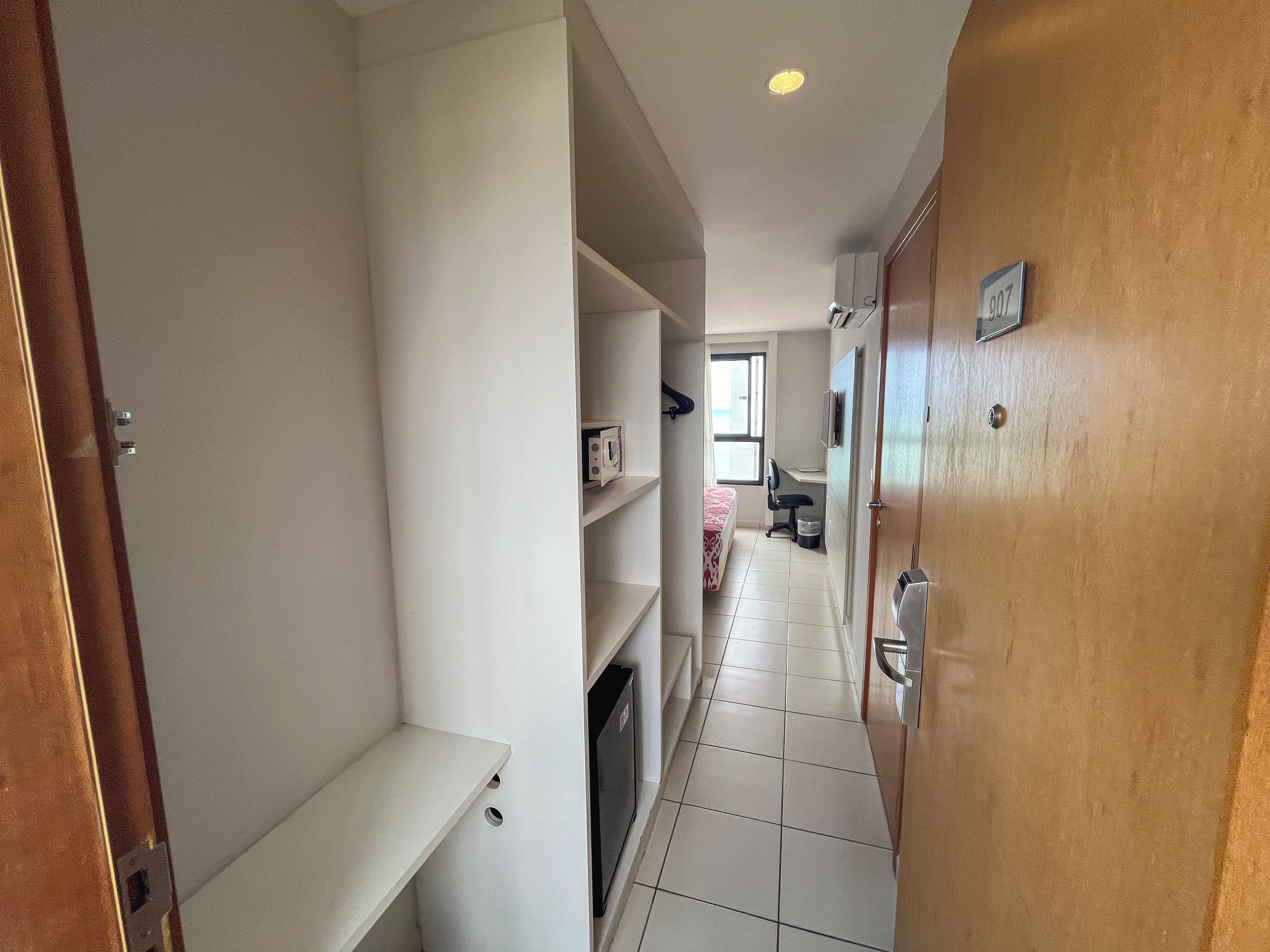 A narrow hallway with a bed, a chair, and a desk area.