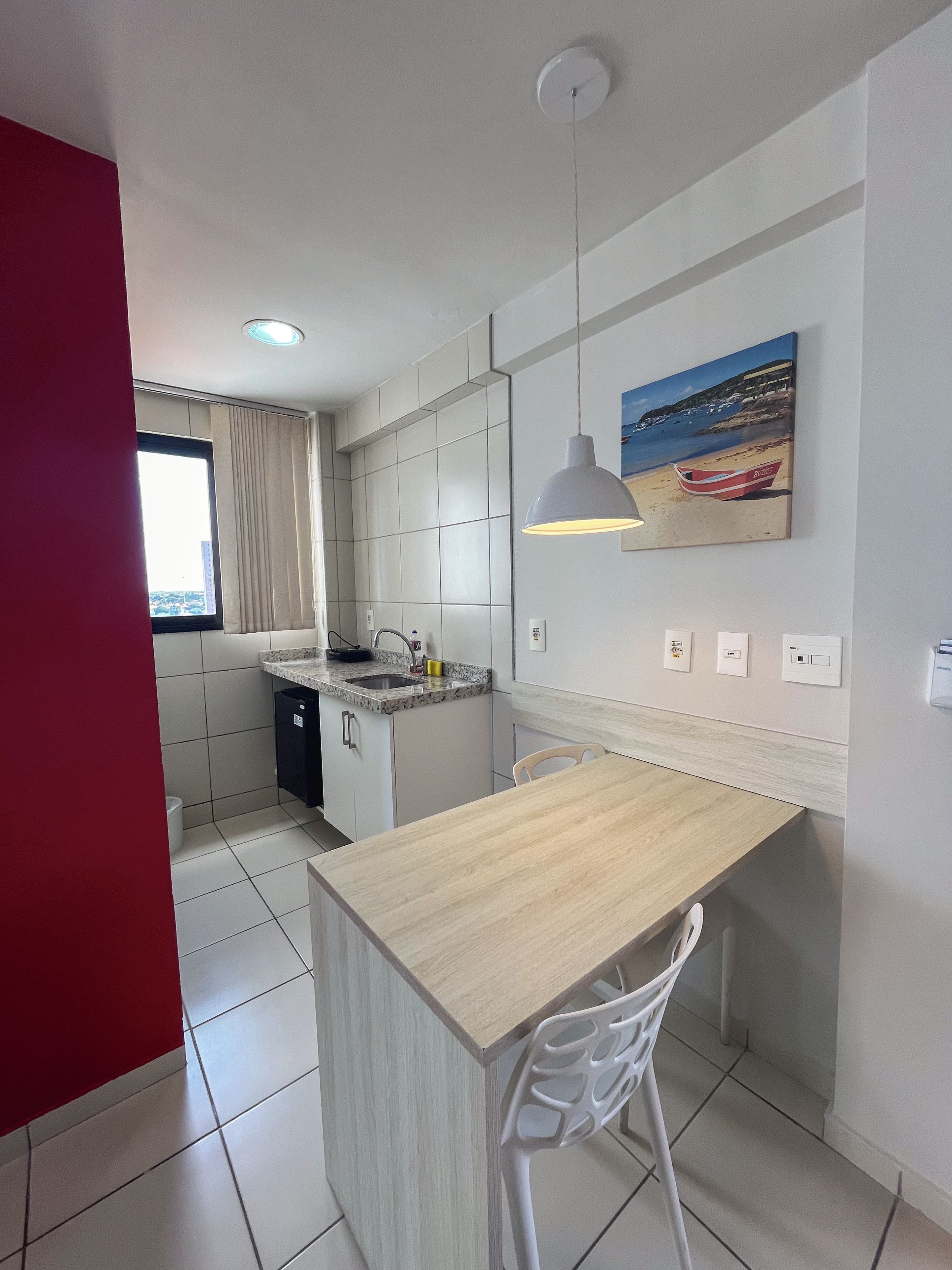 A modern kitchen with white cabinets, a marble countertop, a hanging pendant light, and a painting of a beach scene.