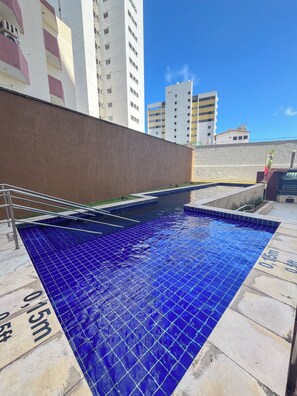 A swimming pool with blue tiles, surrounded by a concrete wall and a metal railing. - Flats Vista Mar (Natal)
