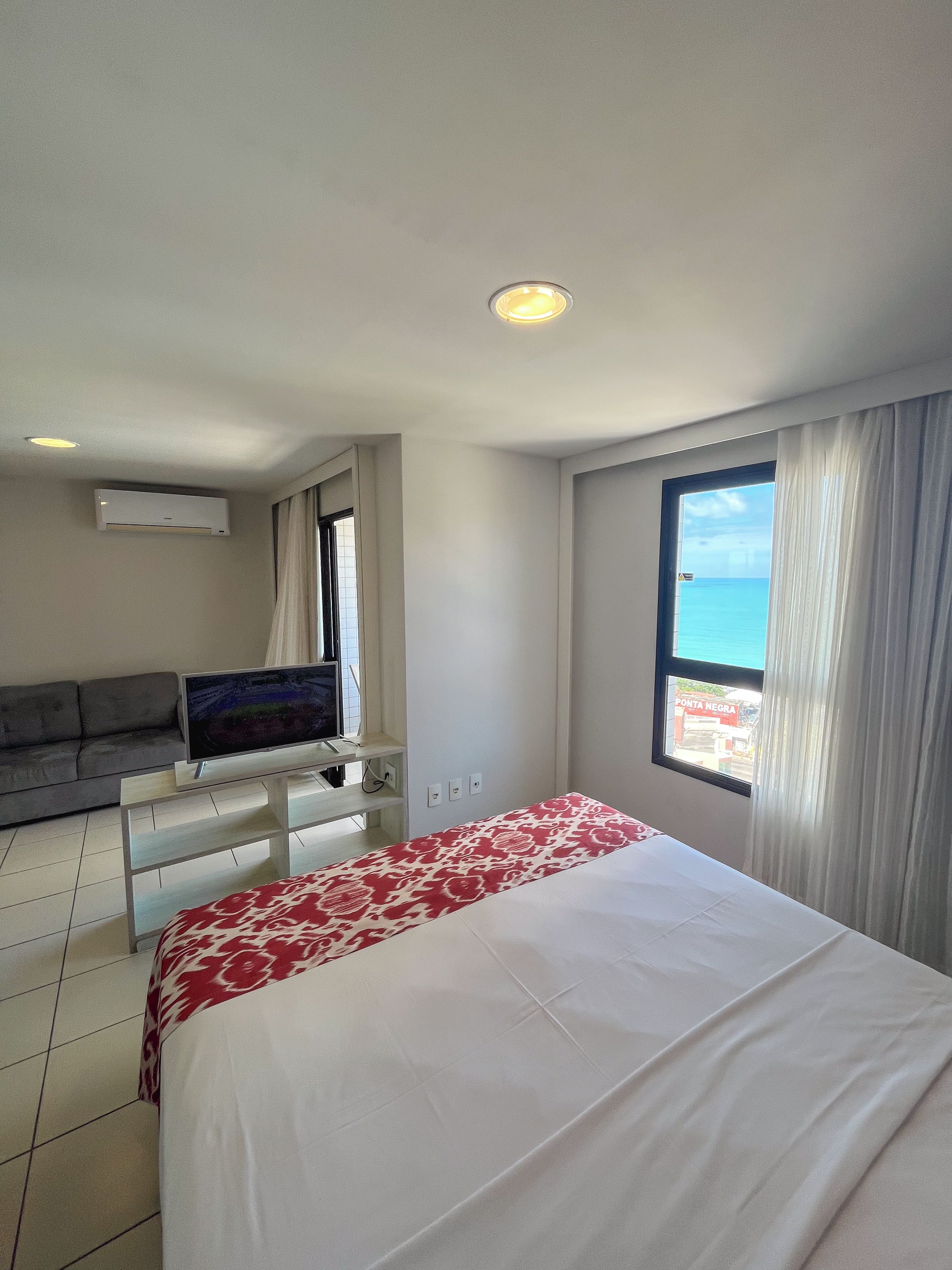 A hotel room with a bed, a sofa, a TV, and a window with a view of the sea.