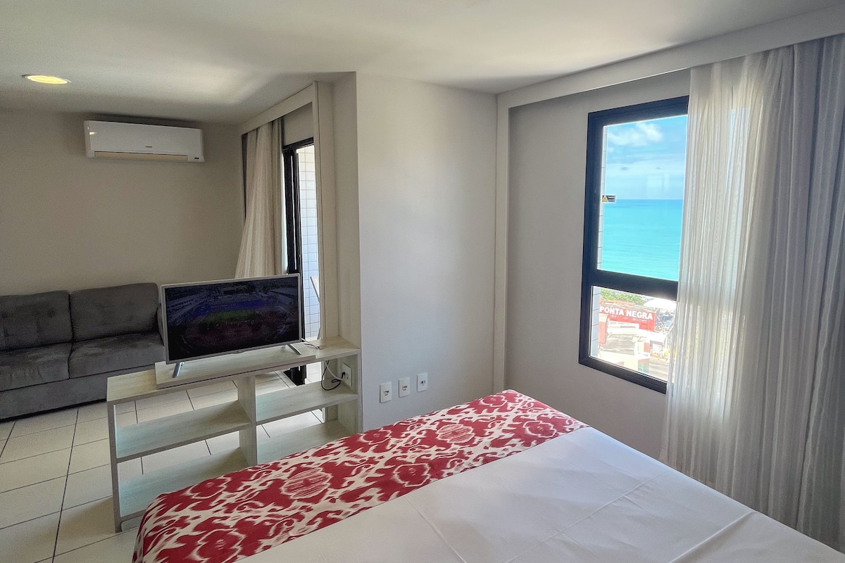 Una habitación de hotel con cama, sofá, televisión y ventana con vista al mar.