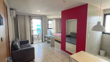 Habitación de hotel moderna con sofá, mesa de comedor con sillas, espejo y vista al mar por la ventana.