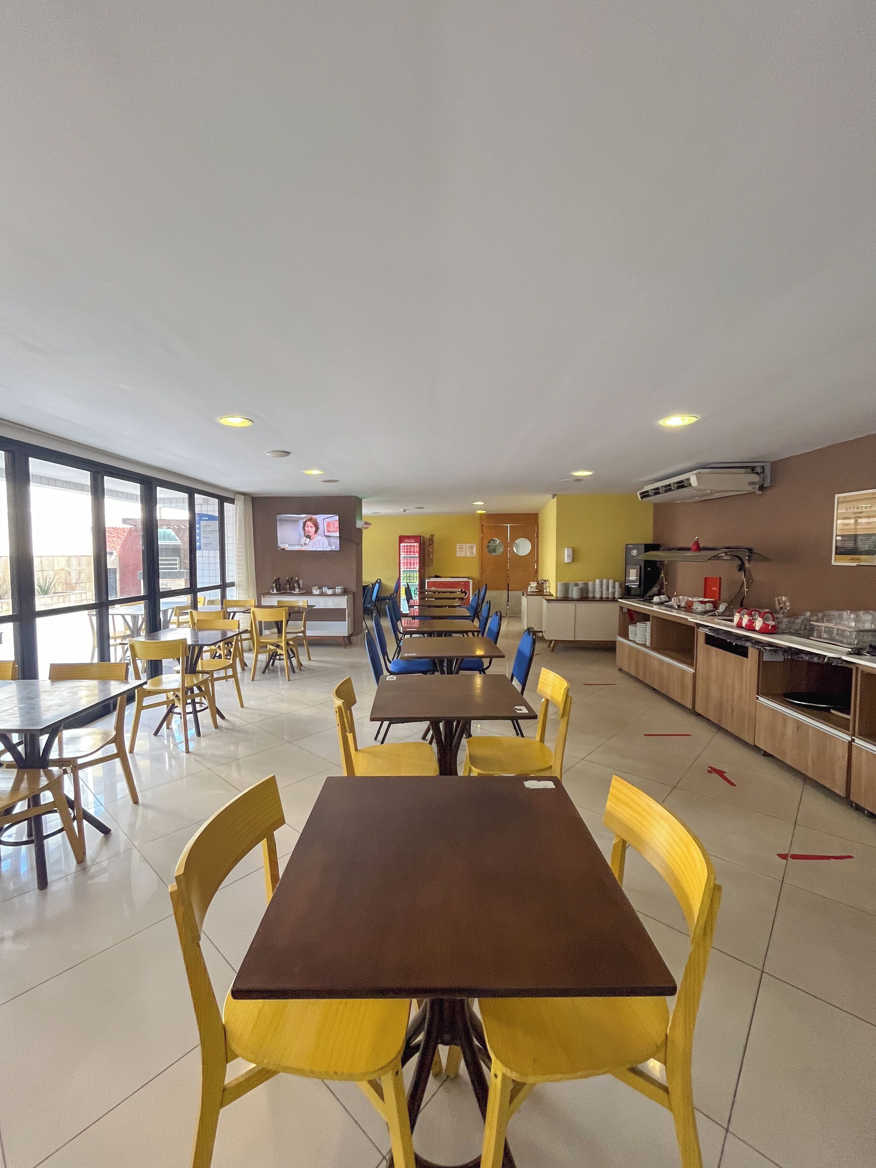 A spacious indoor dining area with multiple tables and chairs, a kitchen area, and a television screen.