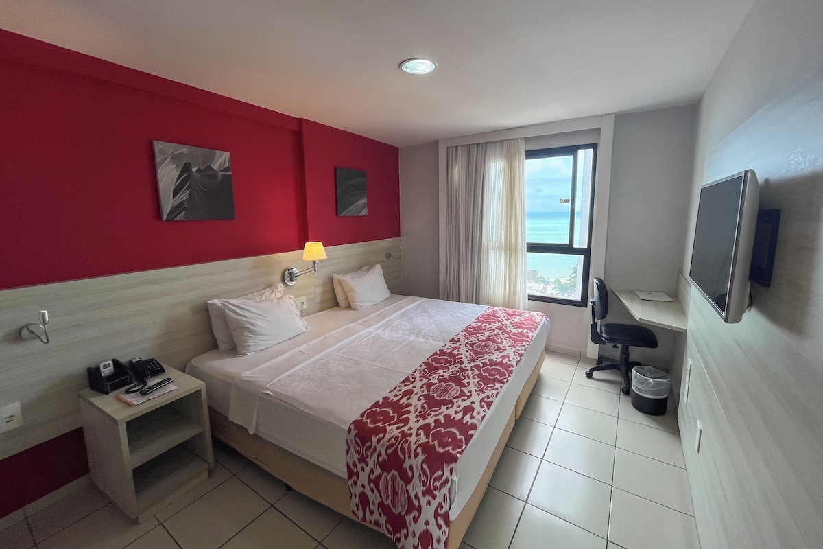 A hotel room with a bed, bedside table, lamp, and a TV.