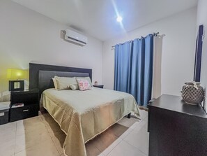 Habitació d'hotel amb llit, una tauleta de nit, aire condicionat, làmpada i un vas decoratiu.