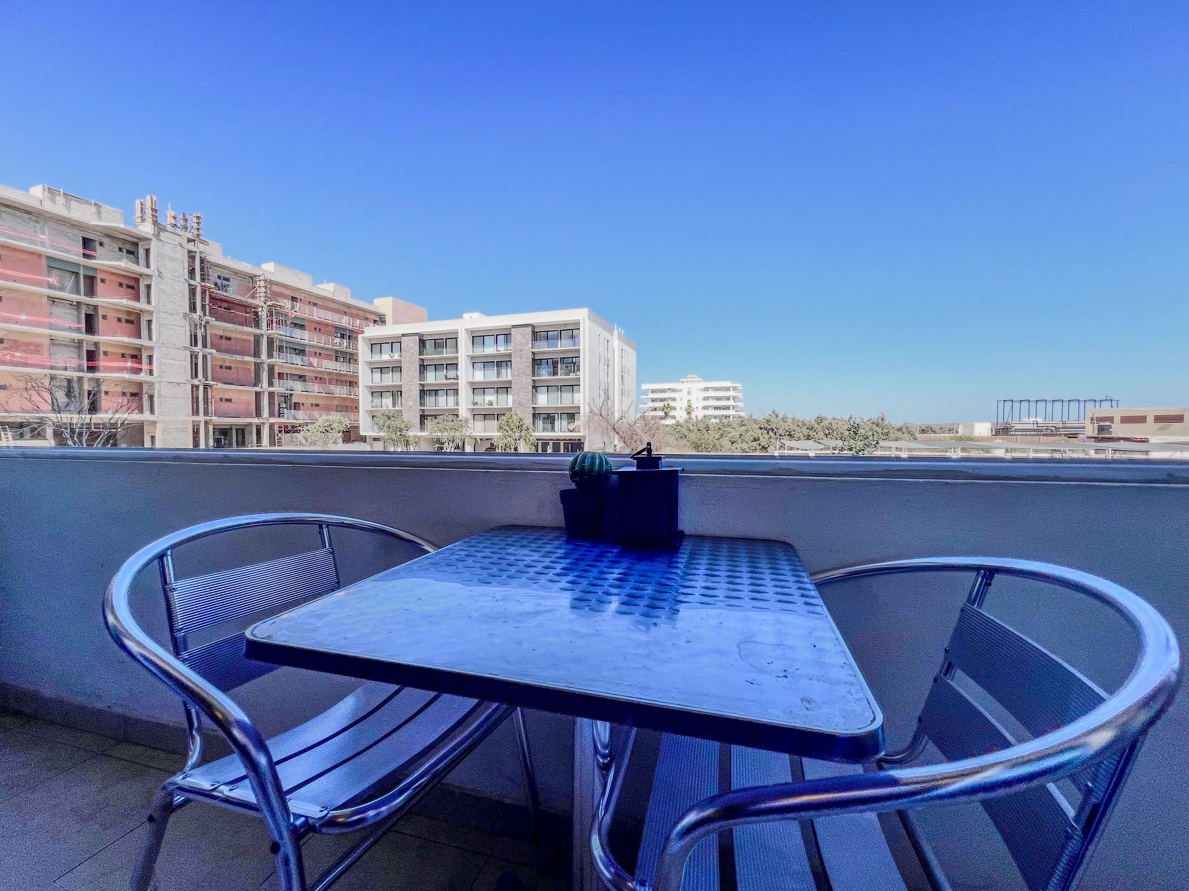 A rooftop terrace with a table and chairs, overlooking a cityscape with buildings.