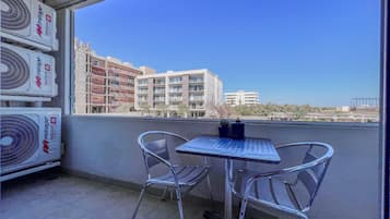 Un balcón con dos sillas de metal y una mesita pequeña, con vista a un paisaje urbano con edificios y cielos despejados.