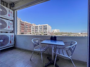 A balcony with two metal chairs and a small table, overlooking a cityscape with buildings and clear skies. - Elegant 2BR/2BA Condo w/ Rooftop Pool, Cabo (Cabo San Lucas)