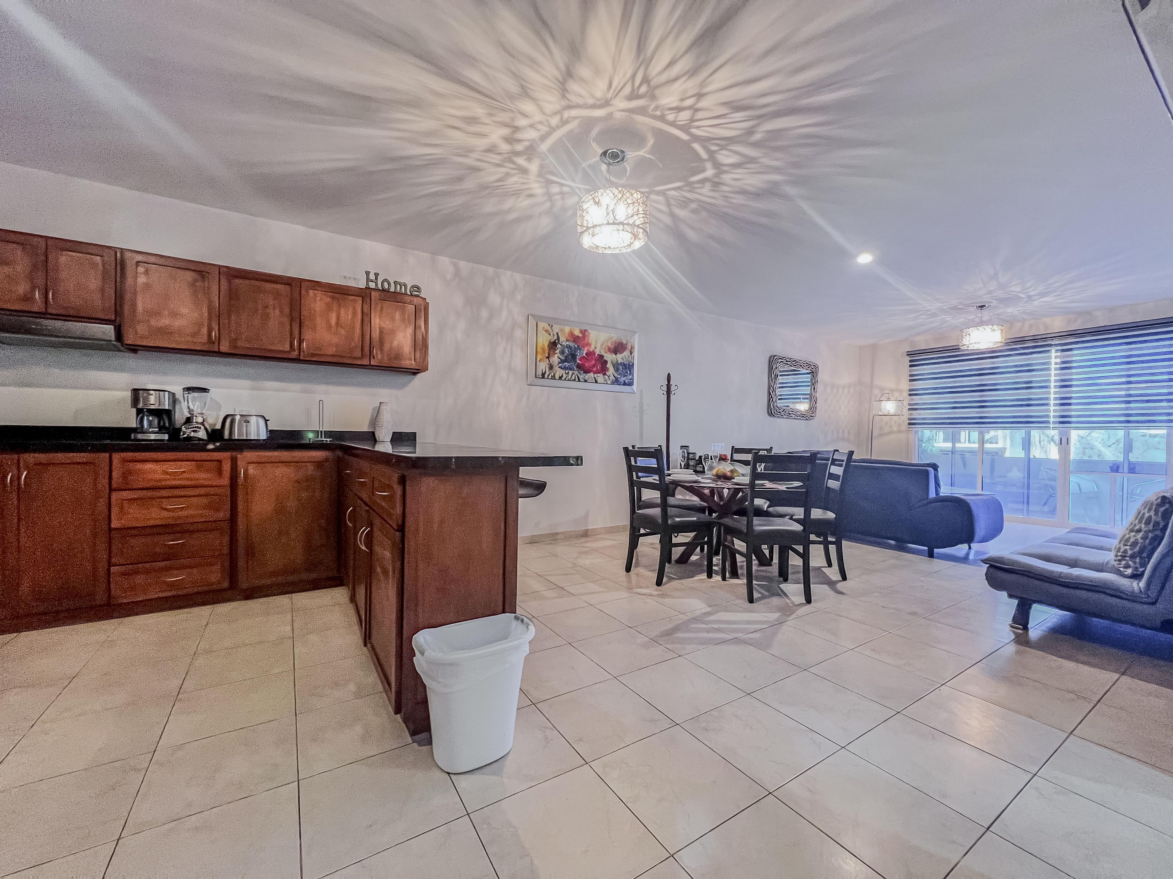 A modern kitchen with wooden cabinets, a dining area with a table and chairs, and a living area with a sofa.