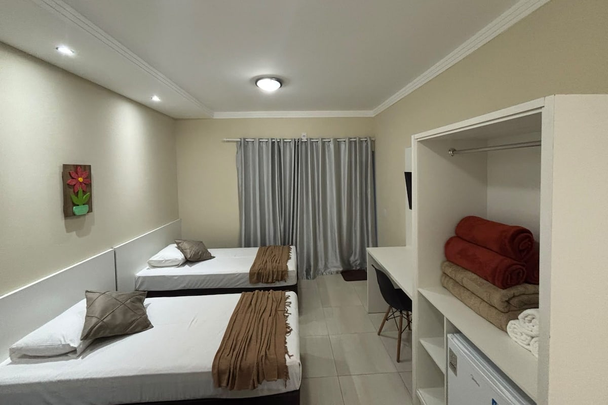 A hotel room with two beds, a desk, a chair, and a wardrobe.