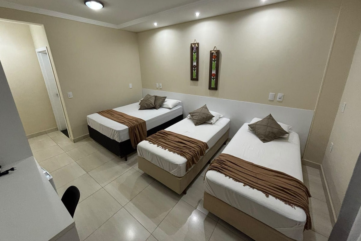 A hotel room with three single beds, a desk, and a chair.