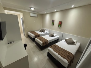 A hotel room with three beds, a TV, and a white desk. - POUSADA DA JAKE PRIME (Penha)