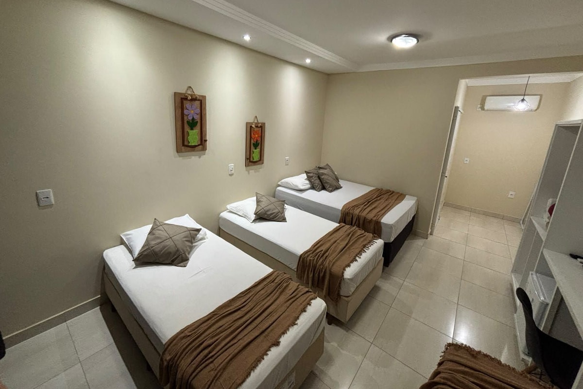 A hotel room with three single beds, a small desk, and a television.
