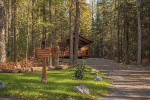 Eine Lodge mit Holzfassade, umgeben von einem Wald. Ein Schild weist auf den Namen der Lodge und nahegelegene Sehenswürdigkeiten hin.