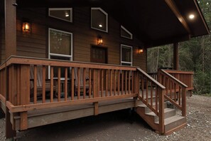 Eine Holzhütte mit überdachter Veranda, einer Treppe und Blick auf den umliegenden Wald.