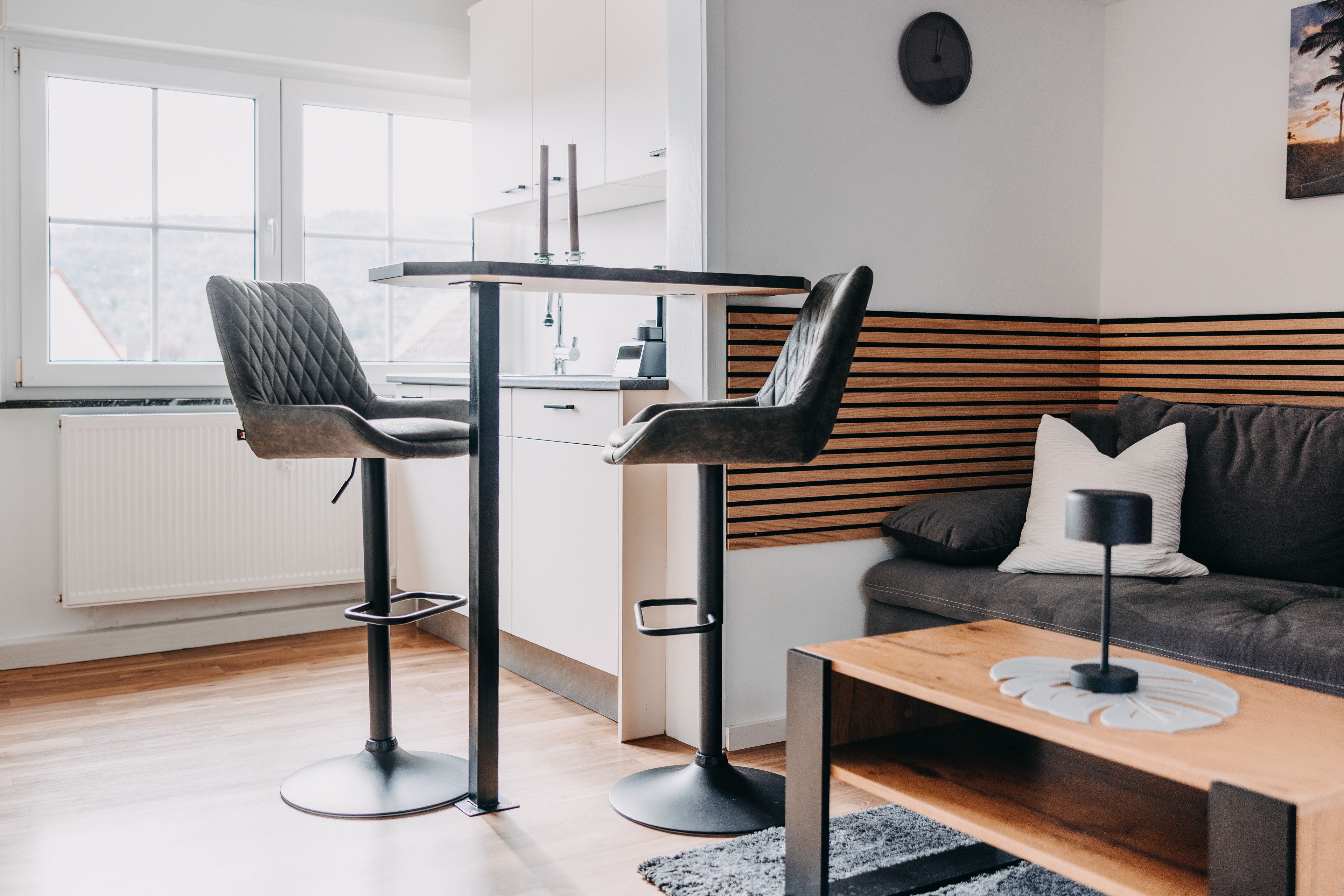 Un espacio habitable moderno con cocina, dos taburetes, un sofá y una mesa de centro.