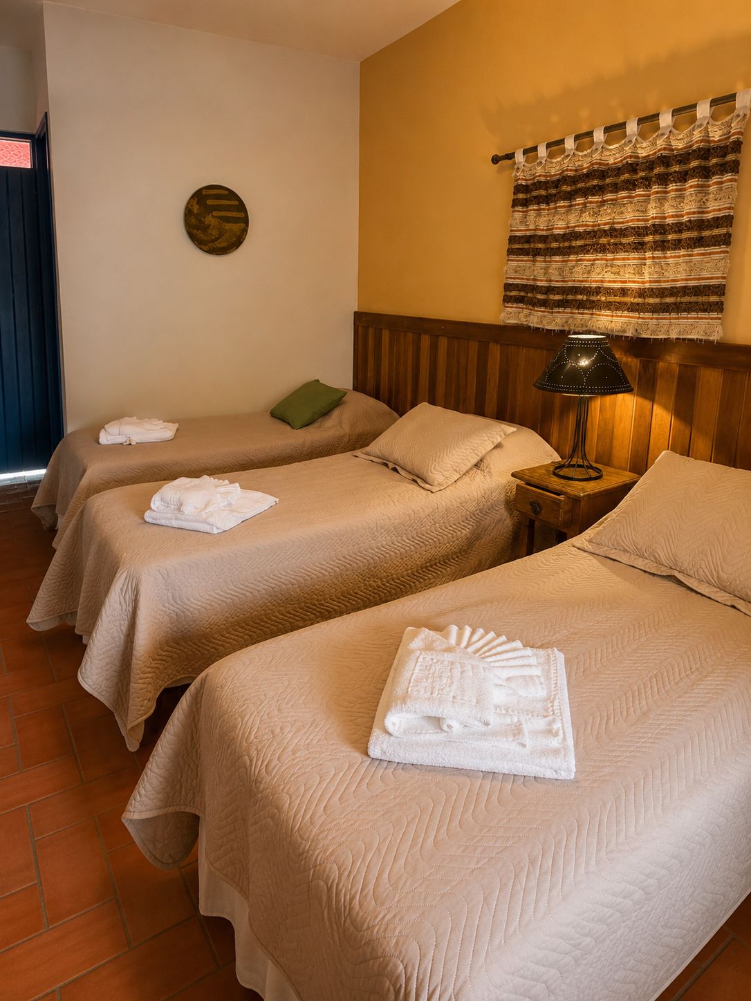 Habitación de hotel con dos camas, cada una con una toalla blanca doblada con esmero, cabecero de madera, lámpara de pared y cortina estampada.