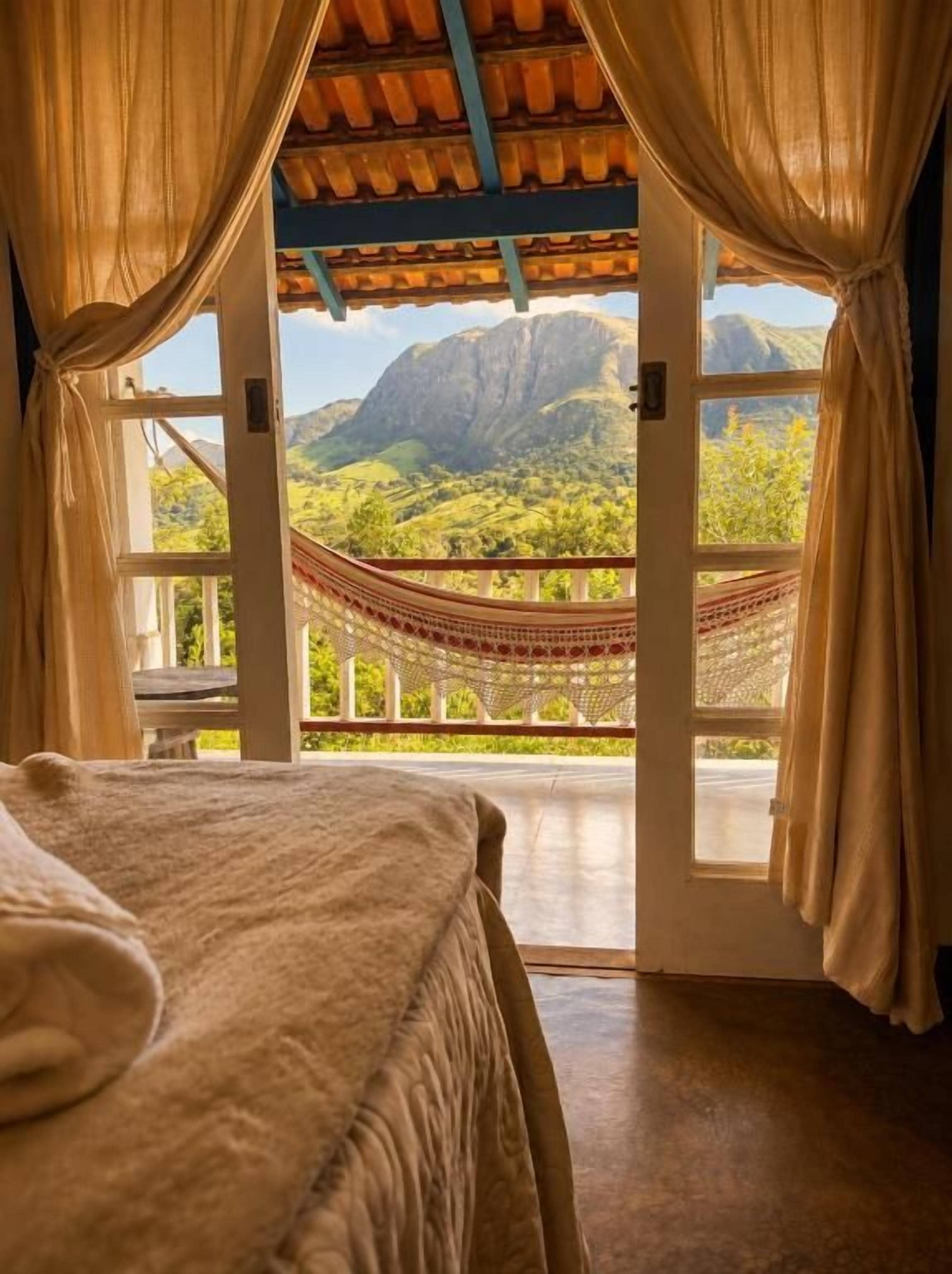 Une pièce avec un lit, un hamac et une vue sur les montagnes, visible à travers une porte ouverte.