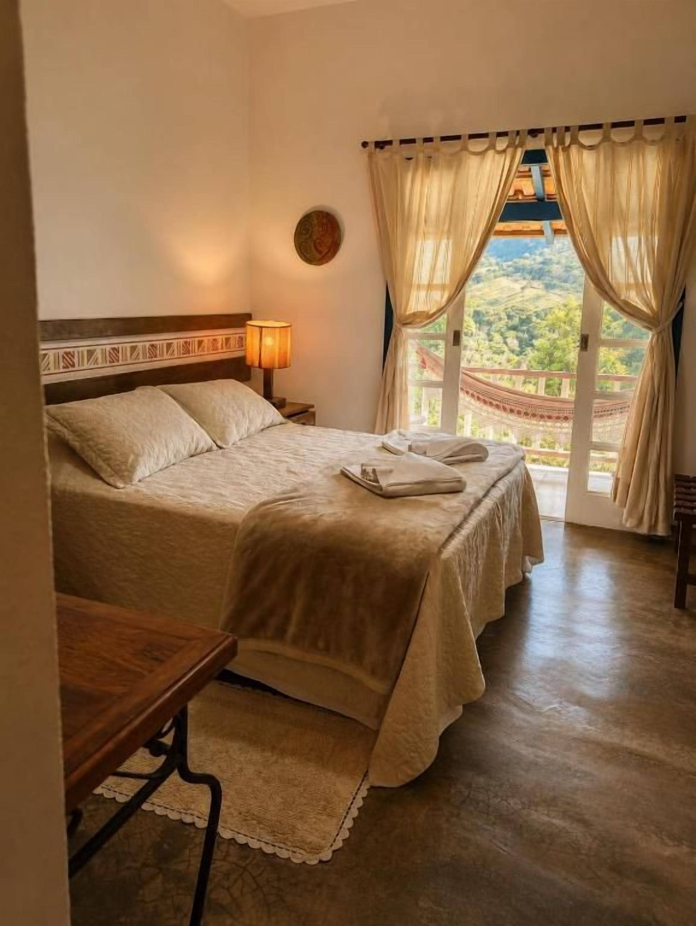 A bedroom with a bed, bedside table, lamp, and curtains.