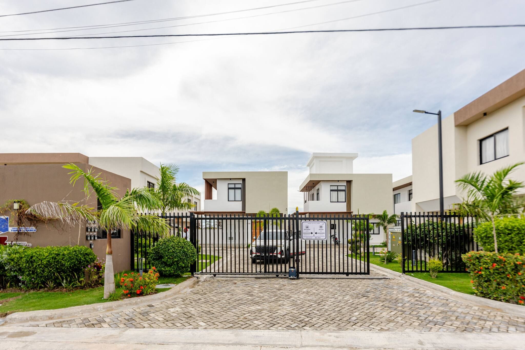 A gated entrance to a residential area with modern buildings, a paved driveway, and well-maintained landscaping.