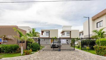 A gated entrance to a residential area with modern buildings, a paved driveway, and well-maintained landscaping.
