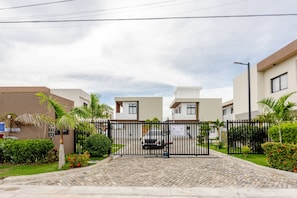 A gated entrance to a residential area with modern buildings, a paved driveway, and well-maintained landscaping. - Beautiful Place 12 Minutes From Airport (Punta Cana)