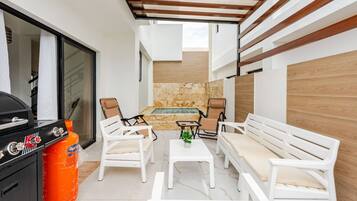 A patio area with a barbecue grill, two white sofas, a small table, and a hot tub.