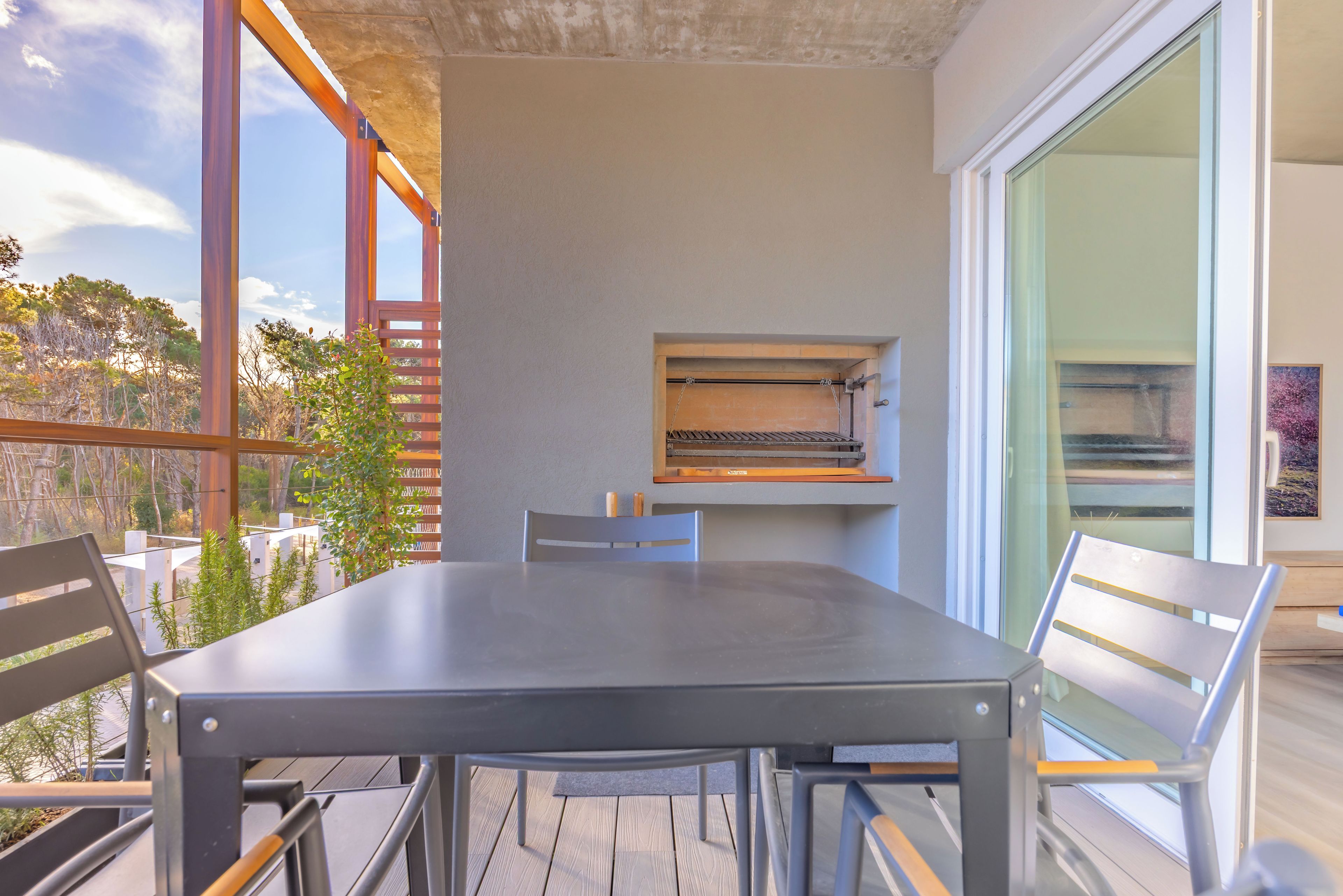 An outdoor dining area with a table and chairs, a pizza oven, and a view of trees and sky.