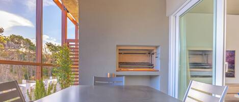 An outdoor dining area with a table and chairs, a pizza oven, and a view of trees and sky.