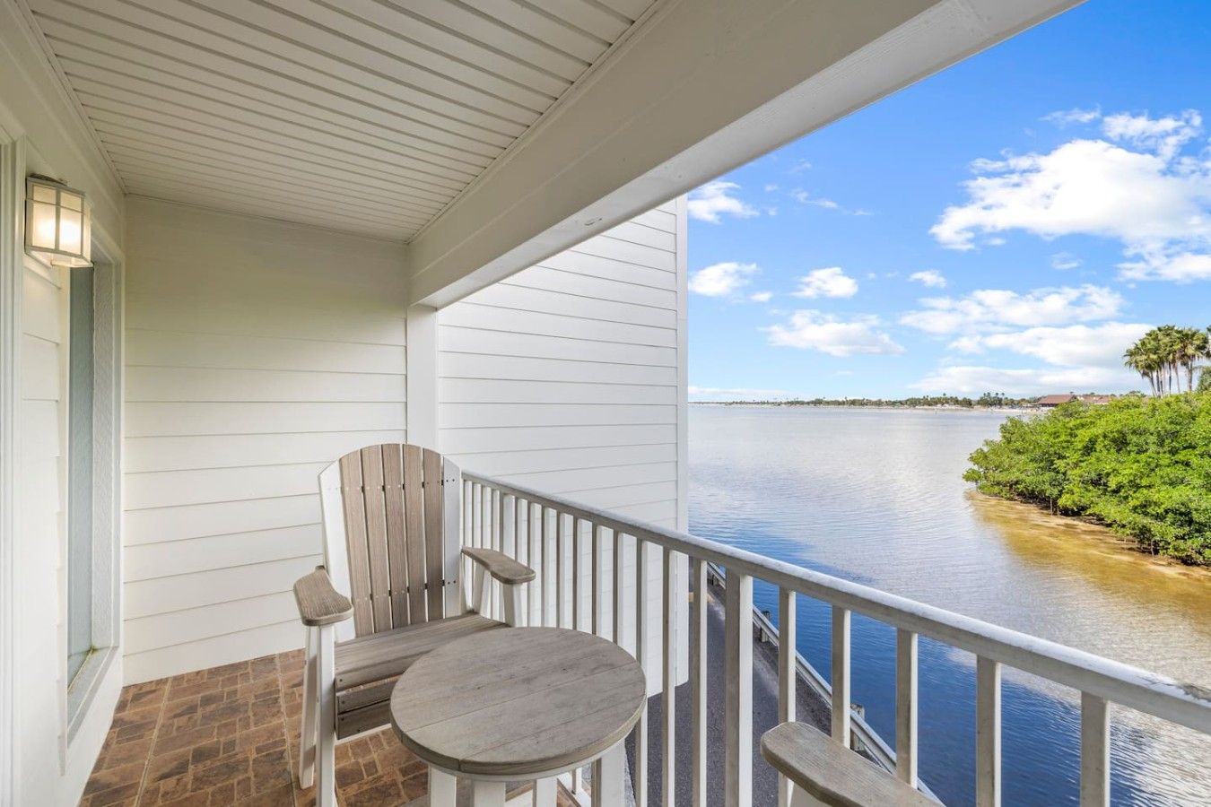 A balcony with a view of a calm body of water, a wooden chair, and a small round table.