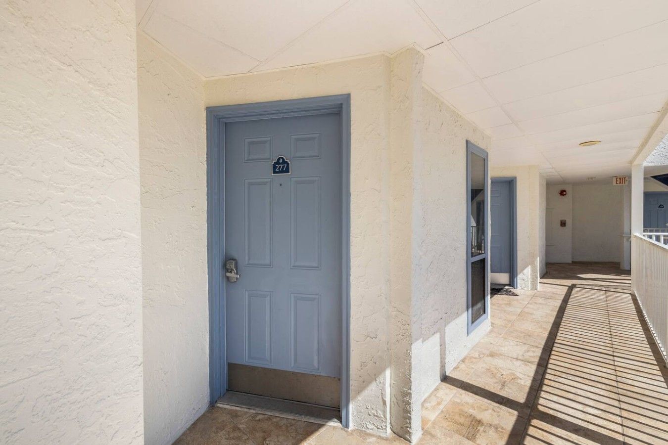 A corridor with a blue door, a white textured wall, and a tiled floor.
