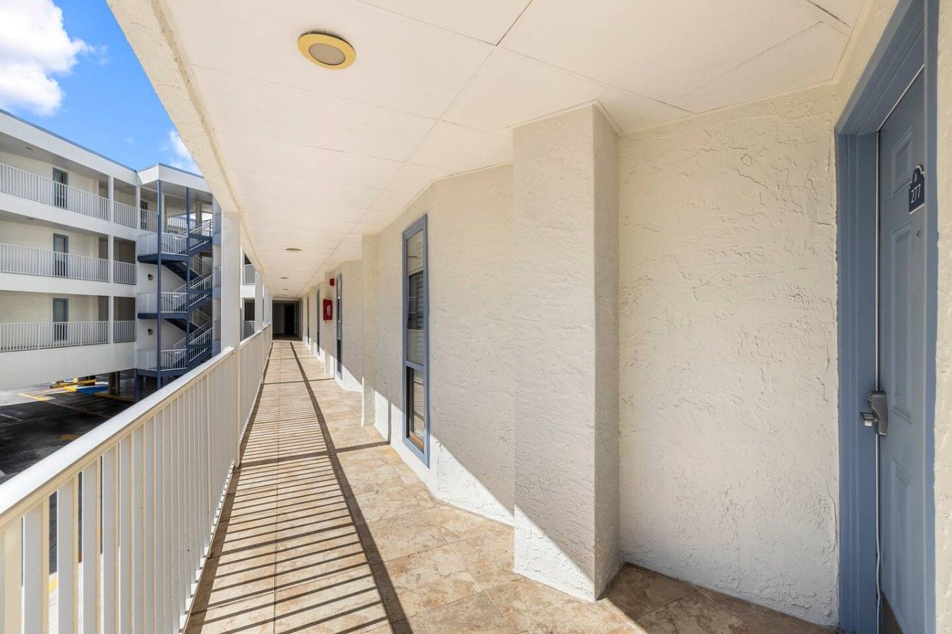 A corridor with a tiled floor, a railing on one side, and a door on the other.