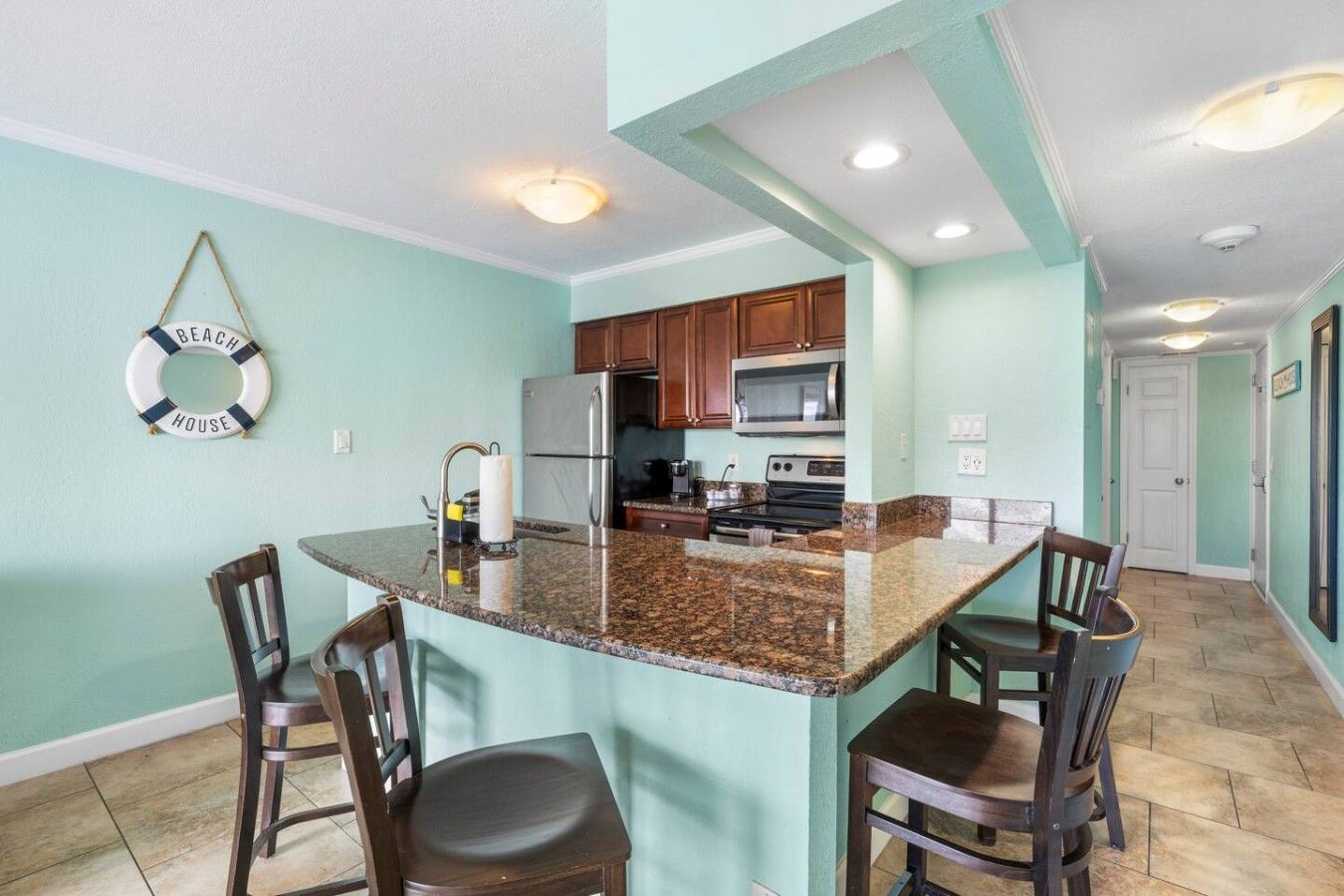 A kitchen with granite countertops, wooden chairs, a stainless steel refrigerator, and a microwave.