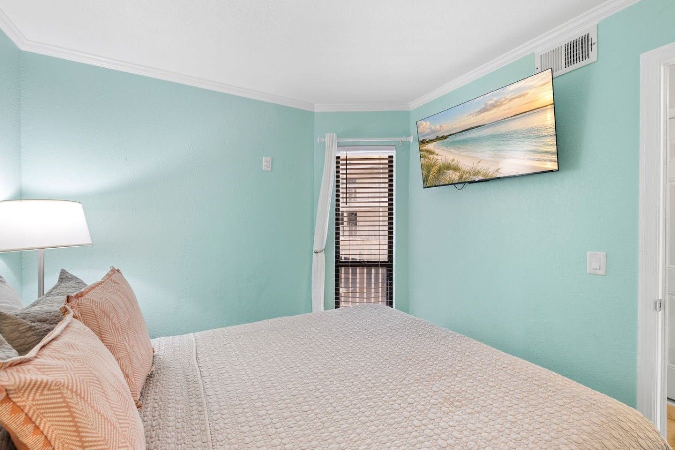 A bedroom with a bed, pillows, a lamp, and a painting on the wall.