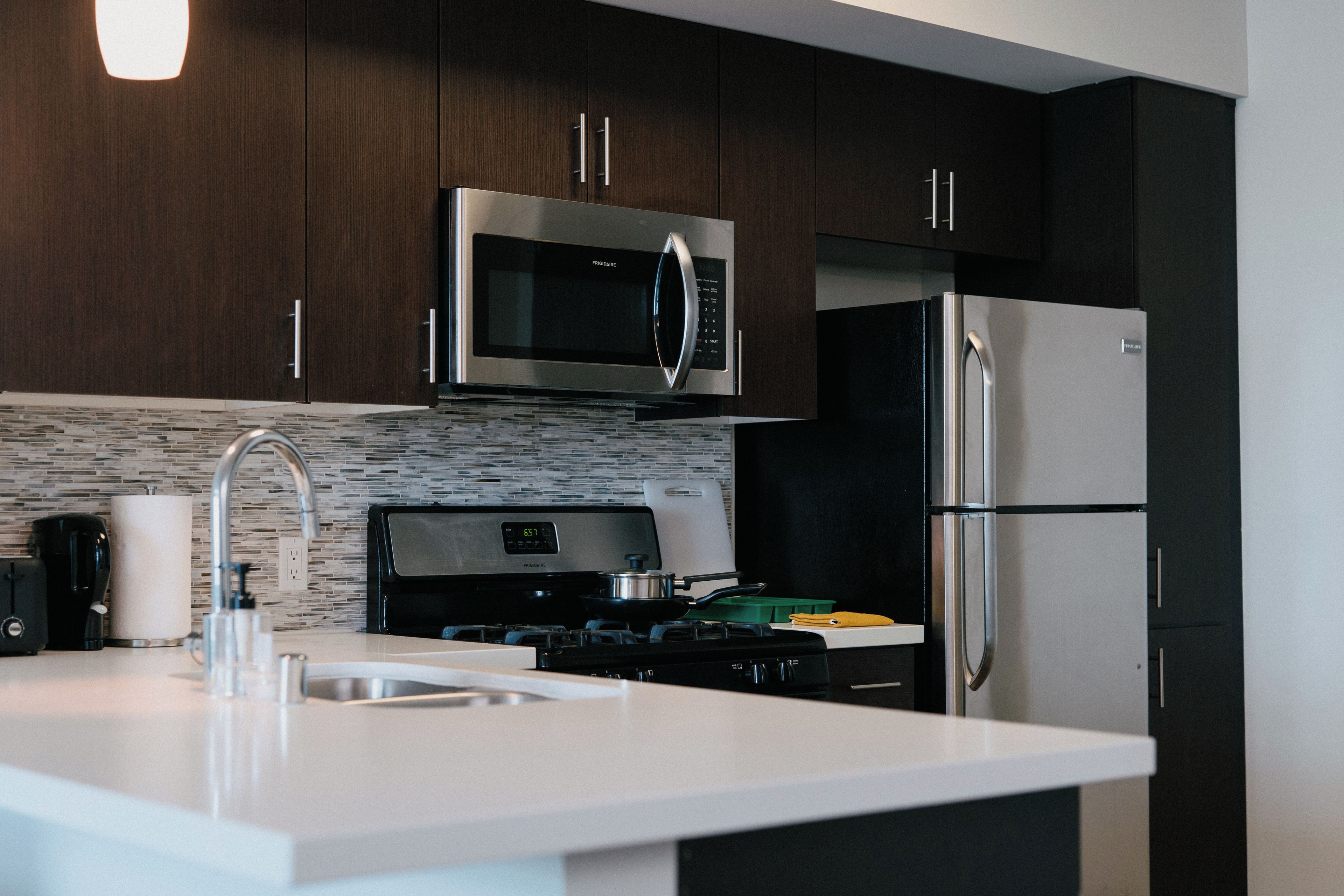 A modern kitchen with dark wooden cabinets, a stainless steel refrigerator, a microwave, and a gas stove.