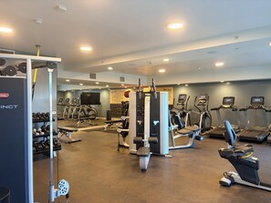 Un gimnasio con cintas de correr, elípticas, equipo de levantamiento de pesas y mancuernas.