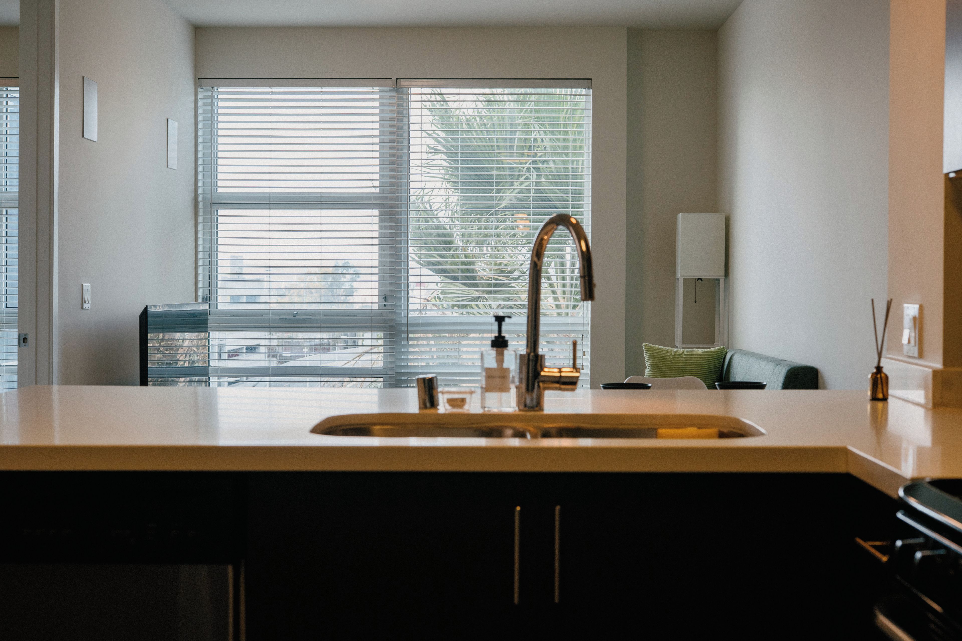 A modern kitchen with a large window, a stainless steel sink, and a green cushion on a couch.