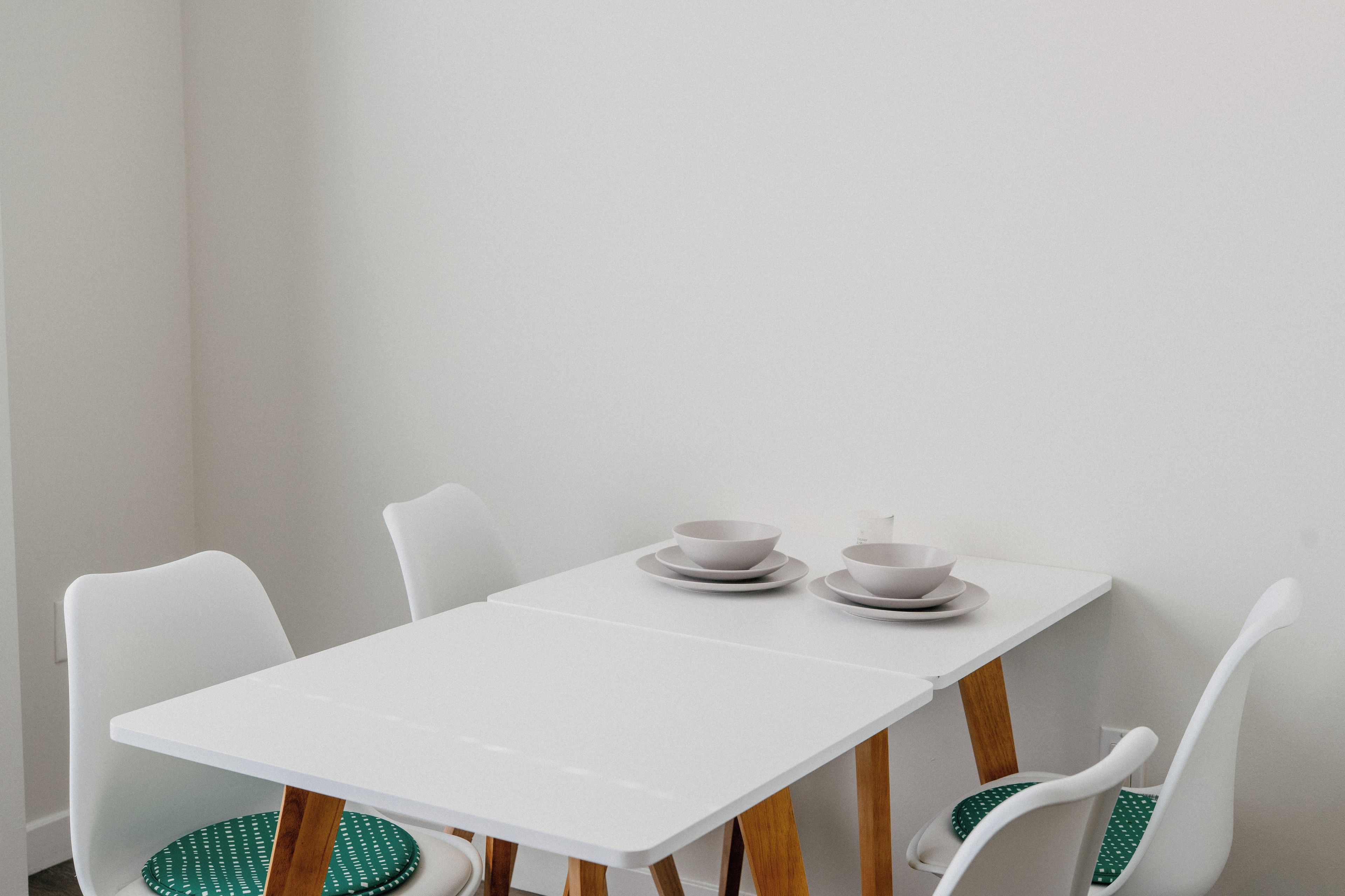 A white table with four chairs, each with a green cushion.
