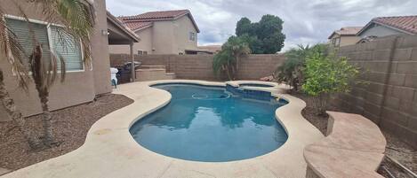 A residential swimming pool with a curved design, surrounded by a brick wall and palm trees.