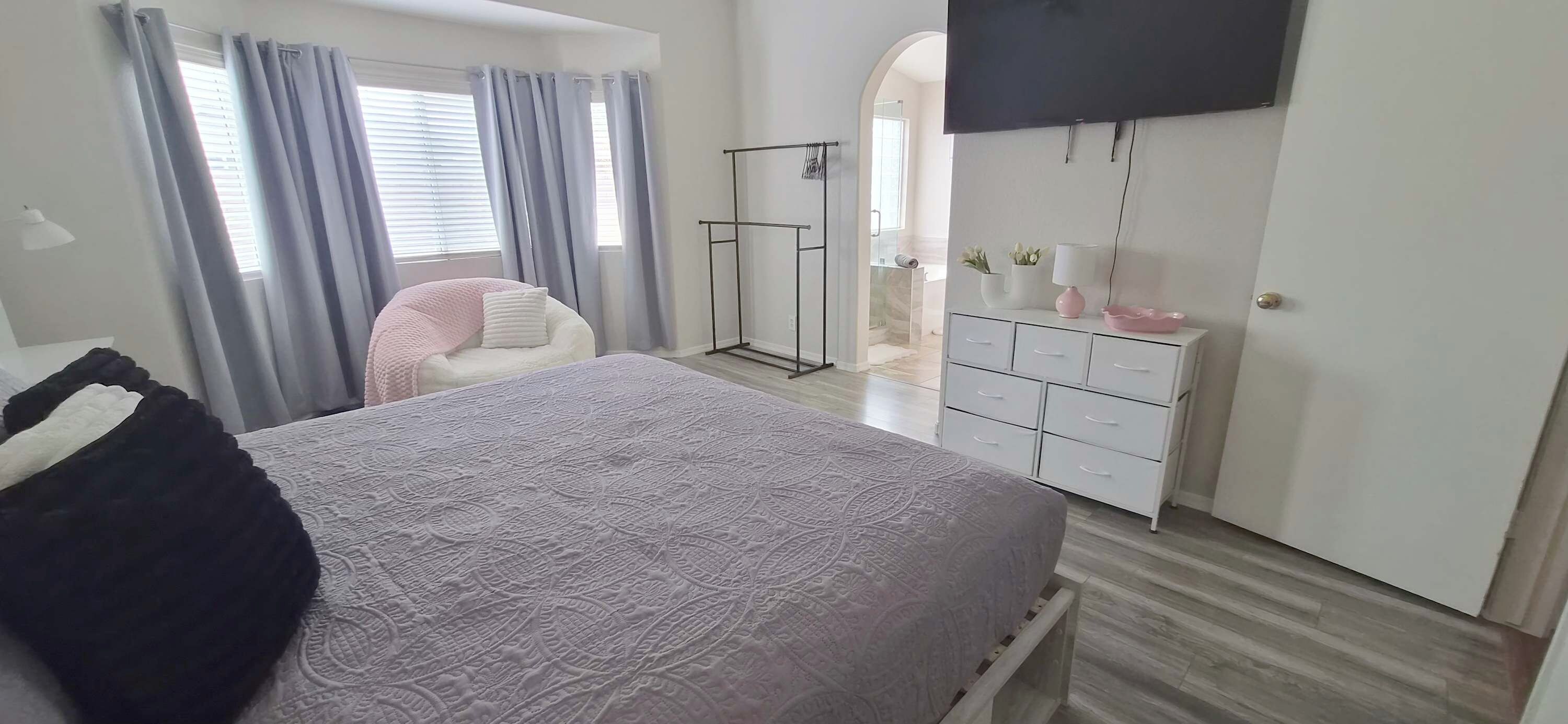 Ein Schlafzimmer mit einem Bett, einem Kleiderschrank, einem an der Wand befestigten Fernseher und einem durch einen Bogen sichtbaren Badezimmer.