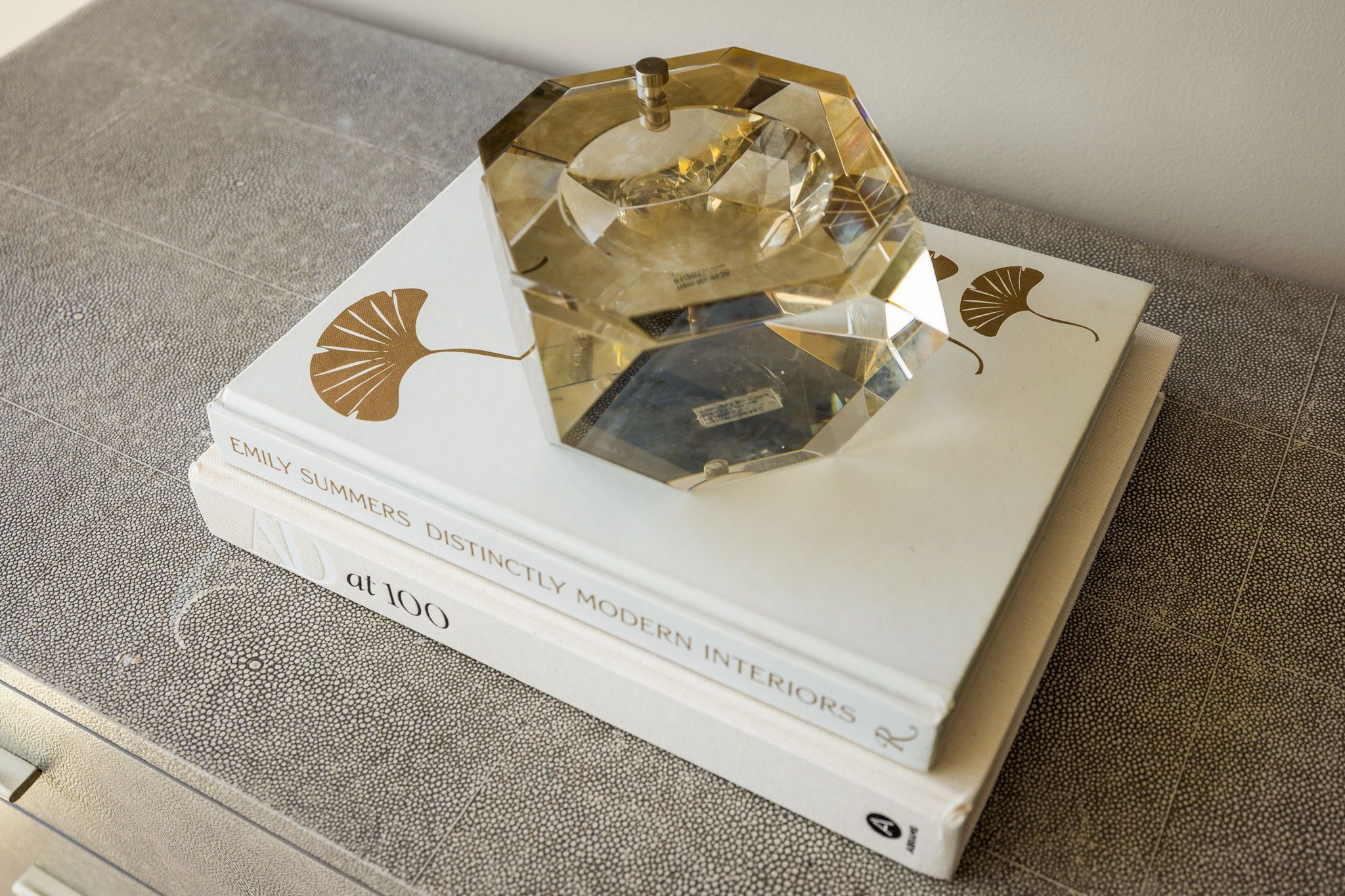 A book titled 'EMILY SUMMERS DISTINCTLY MODERN INTERIORS' with a decorative glass object on top.
