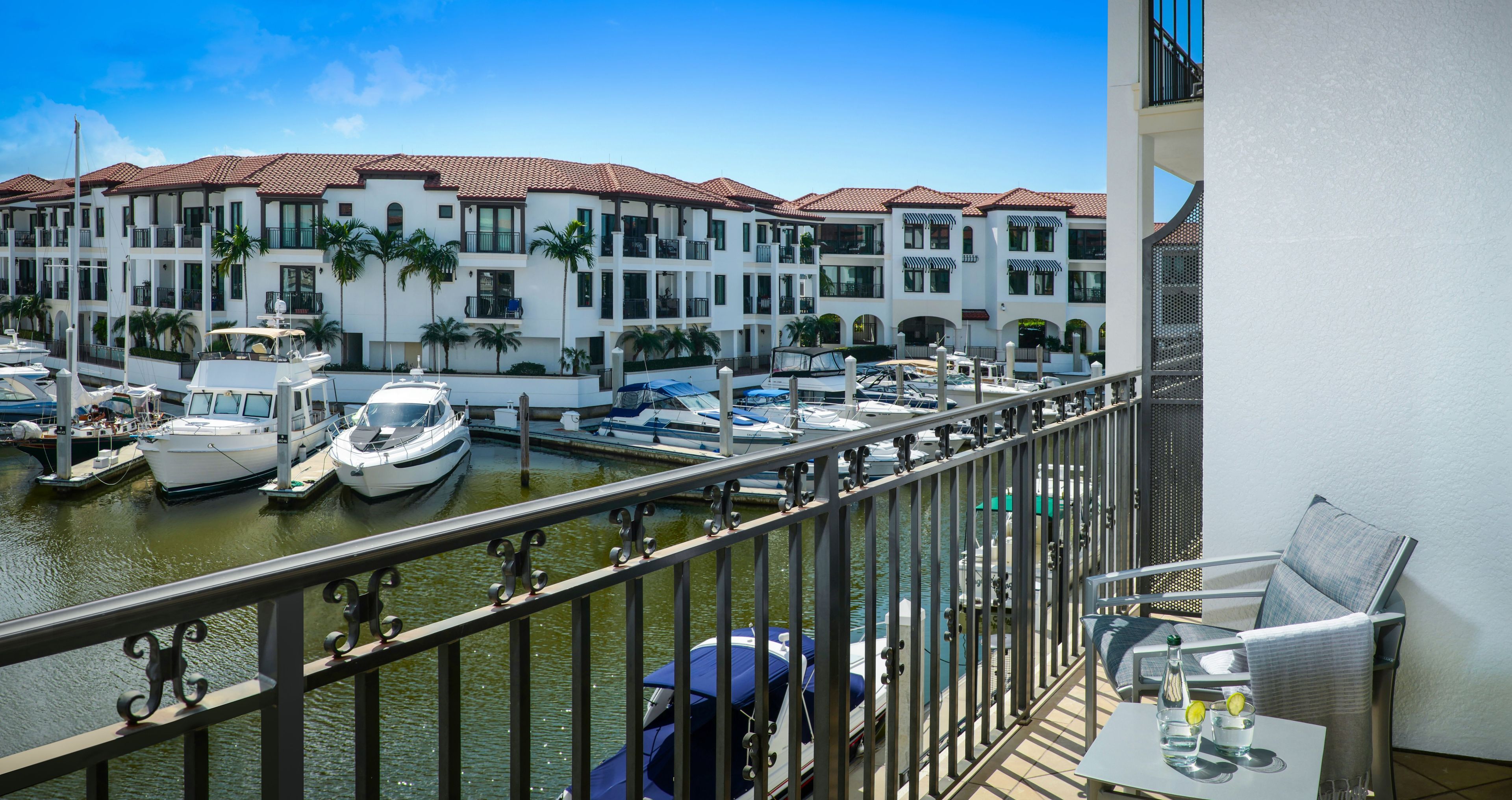 A balcony with a view of a marina, boats docked, and a building with balconies.