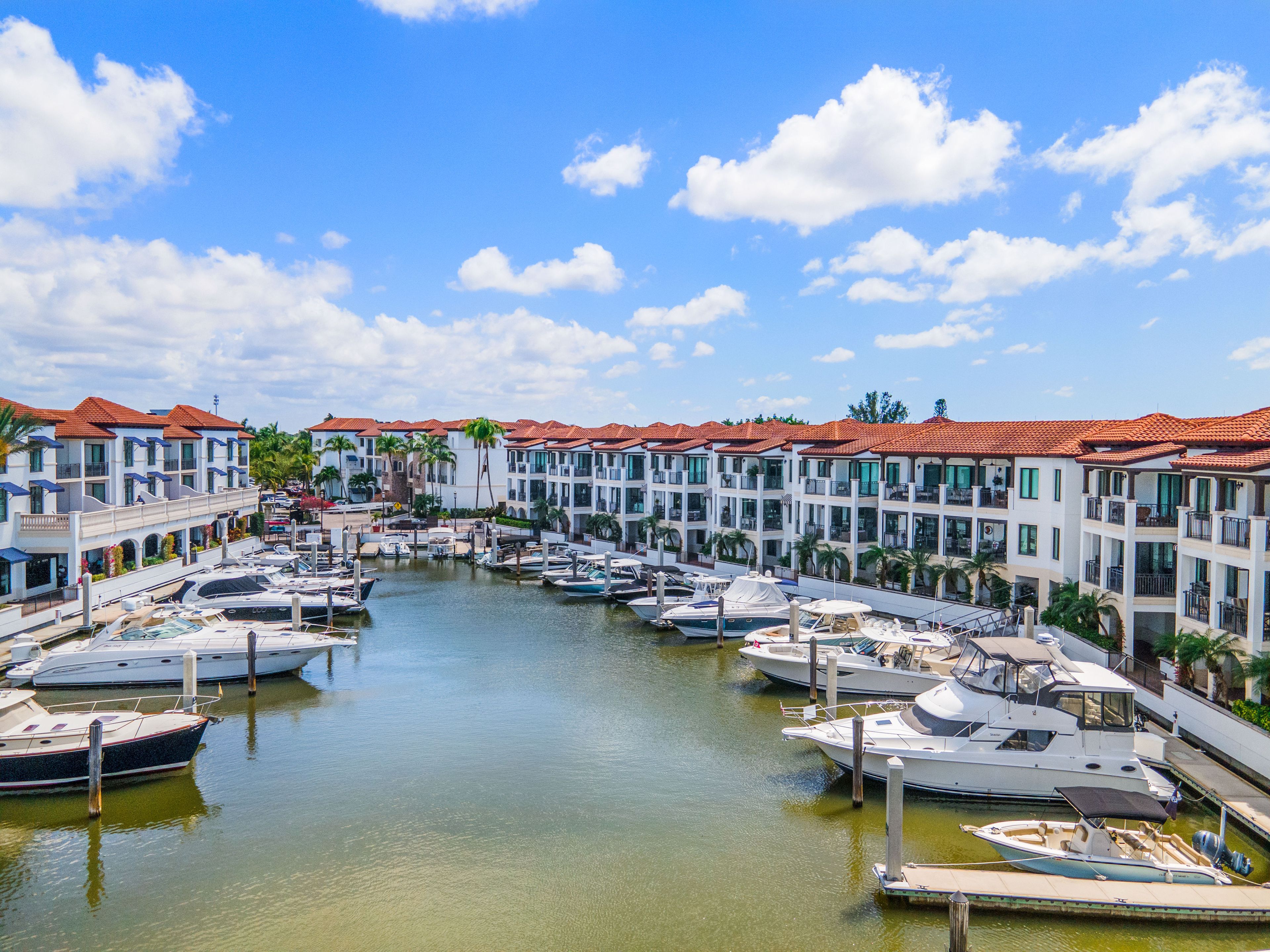 A marina with multiple boats docked, surrounded by buildings with red-tiled roofs.