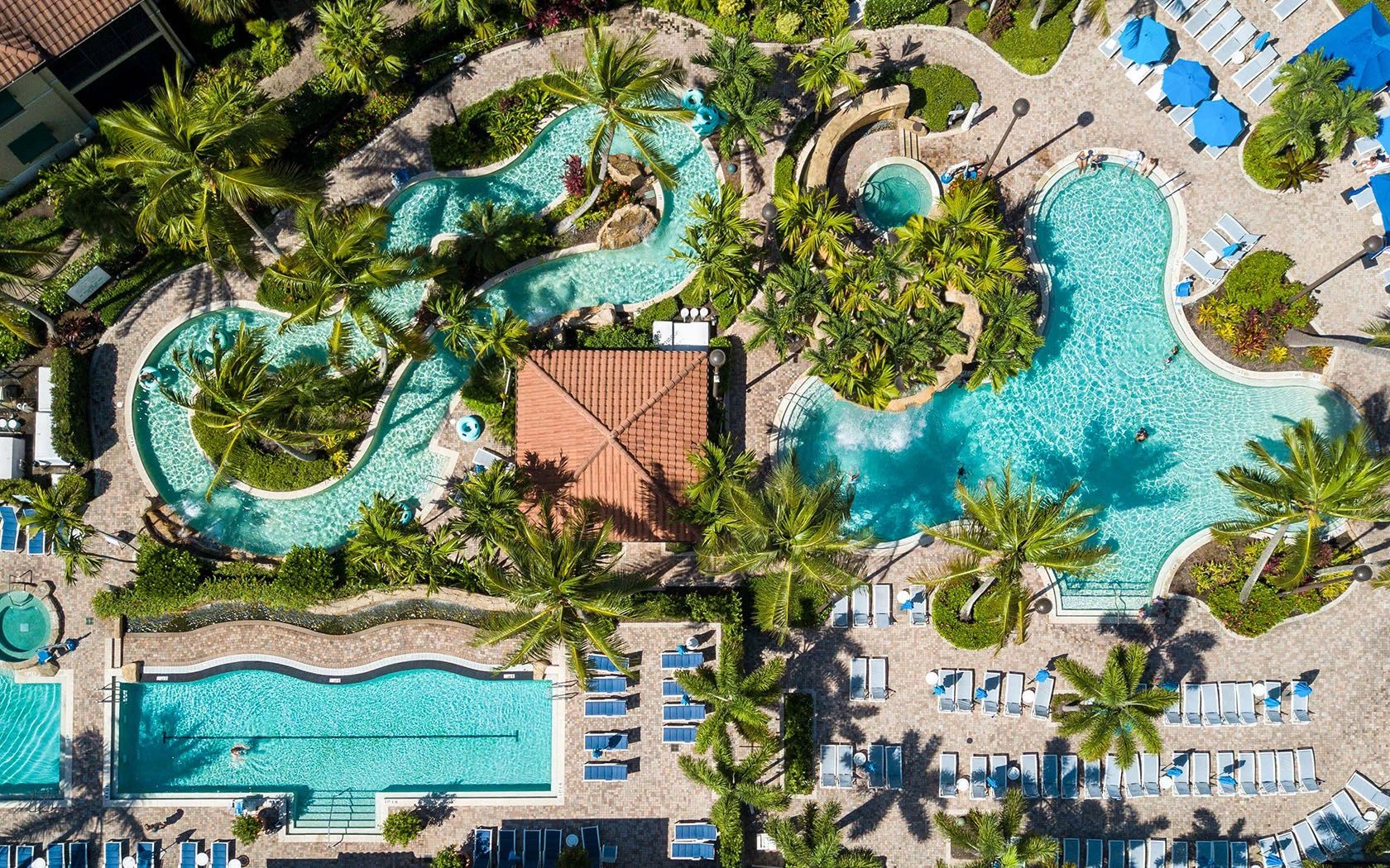 A large, multi-pool resort with various swimming areas surrounded by palm trees and sun loungers.