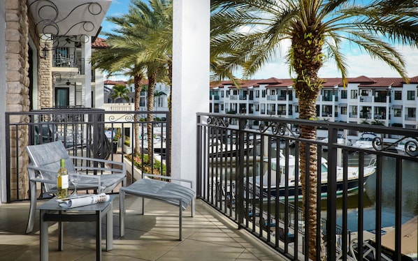 Un balcon donnant sur un port de plaisance, aménagé avec une table, des chaises et une bouteille de vin.