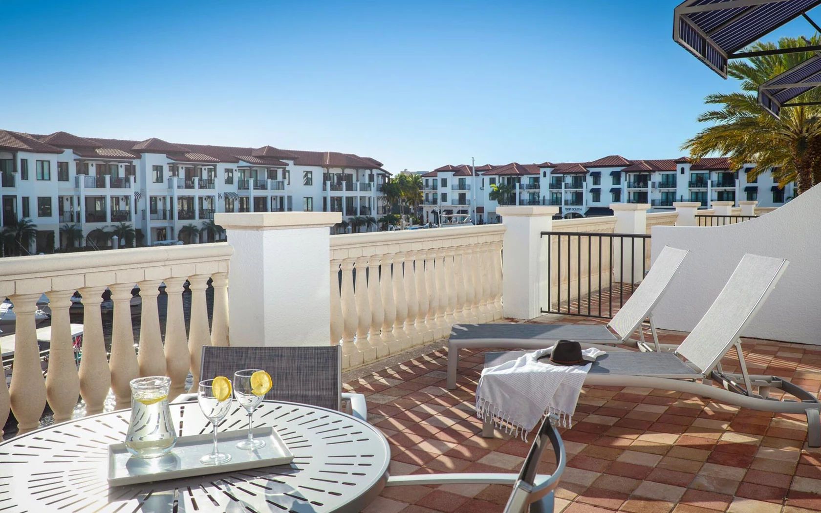 A rooftop terrace with a table set for two, lounge chairs, and a view of hotel buildings.