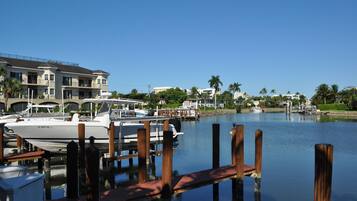 A marina with boats docked, a wooden dock, and a large building with balconies in the background.