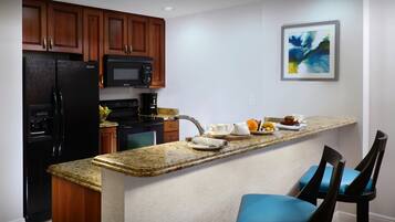 A kitchen with a granite countertop, stainless steel appliances, wooden cabinets, and a painting on the wall.